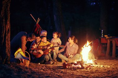 Ormanda güzel bir gecede kamp ateşinin etrafında eğlenen mutlu bir aile.