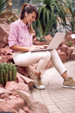 Genç bayan ziyaretçi botanik bahçesinde dizüstü bilgisayarın içeriğini izlerken rahatladı.