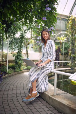 Güzel bir botanik bahçesinde poz veren neşeli genç bir kız öğrenci.