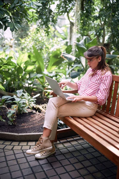 植物園のノートパソコンで植物についてのテキストを読む若い女性生物学の学生 — ストック写真