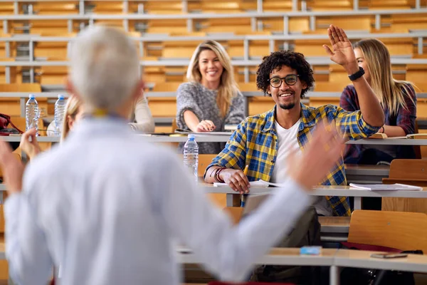 大学の教室での講義で教授の質問に答えるために手を挙げている男性学生 — ストック写真