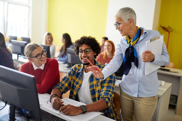 A female professor giving help to students at the informatics lecture in the university computer classroom. Smart young people study at the college. Education, college, university, learning and multiethnic people concep