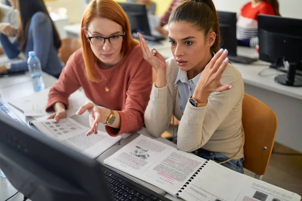 A female student giving help to a colleague at the informatics lecture in the university computer classroom. Smart young people study at the college. Education, college, university, learning and people concept