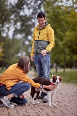 Genç beyaz erkek köpeğinin tasmasıyla güzel dişiye bakıyor, gülümsüyor.