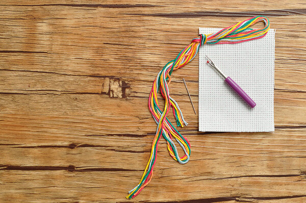 String of colorful embroidery thread displayed with a piece of embroidery fabric, a needle and a picker