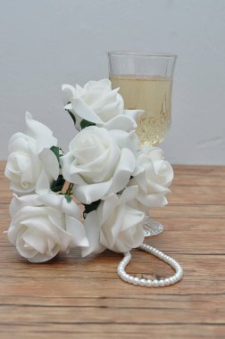 Bir bardak şampanya, beyaz gül ve bir dizi inci