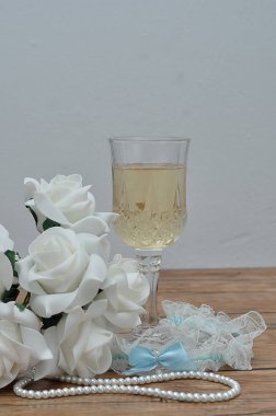 Bir bardak şampanya, beyaz gül, bir dizi inci ve bir jartiyer