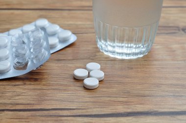 Bir bardak su ve iki blister paketleri ile görüntülenen beyaz hap