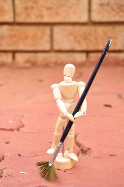 Bir süpürge olarak bir boya fırçası ile ahşap bir manken kaldırım süpürme