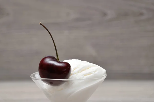 A single cherry on top of a scoop of ice cream in a glass bowl