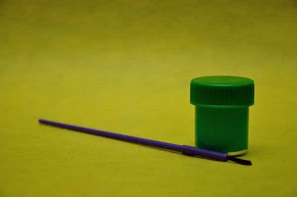 Ein Topf mit grüner Farbe mit einem violetten Pinsel auf gelbem Hintergrund — Stockfoto