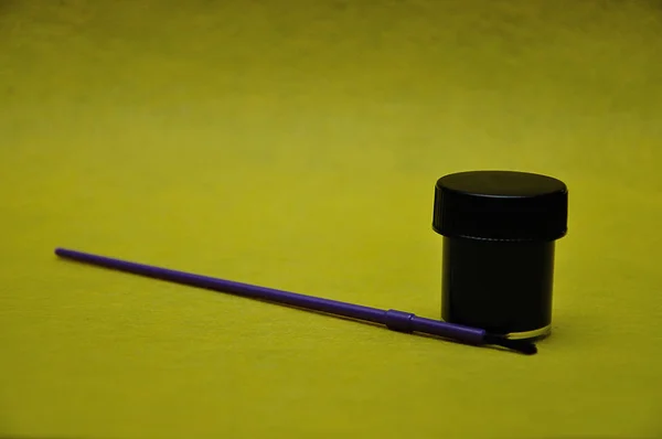 A pot of black paint with a purple paintbrush on a yellow background — Stock Photo, Image