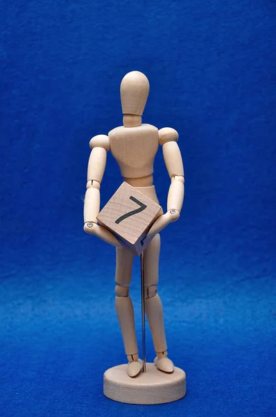 A wooden mannequin with a wooden block with the number seven