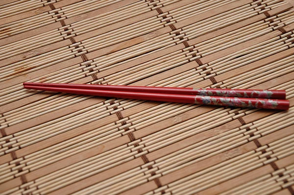 A pair of red chopsticks on a bamboo place mat — Stock Photo, Image