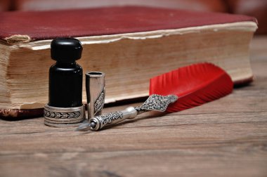 Ahşap bir masanın üzerinde kırmızı bir kitapla bir şişe mürekkep olan eski bir kalem.