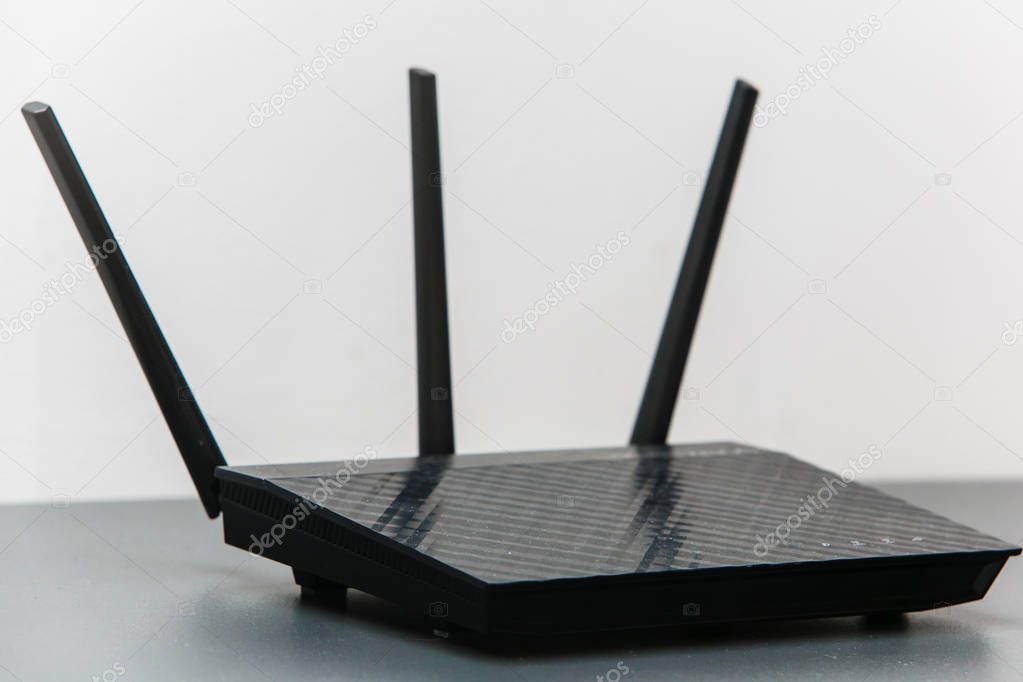 Black router with three antennas in white background. Router close-up