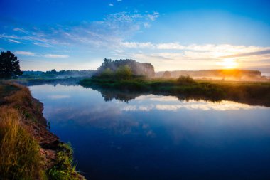 Ufukta parlak güneş ışığı. Sisli nehirde mavi gündoğumu