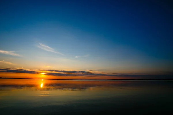 Bright sun rolling down the horizon line. Blue sky over local lake