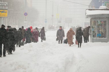 Yayalar ağır blizzard karlı kaldırım boyunca hareket. Otobüs durağında bekleyen adam