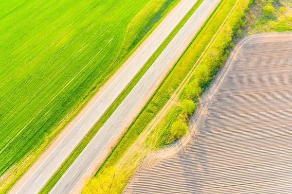 Green fields and dry soil along the road. Aerial landscape in countryside