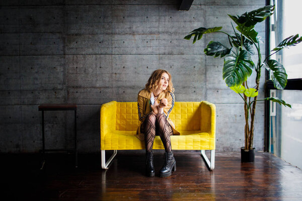 Beautiful blonde sitting on yellow couch. Moving house concept. Choosing furniture. Hesitation notion