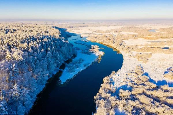 V zimním údolí, v vzdušné krajině, začíná jasný slunečný den. Řeka zatáčí v blízkosti hustého zasněženého lesa — Stock fotografie