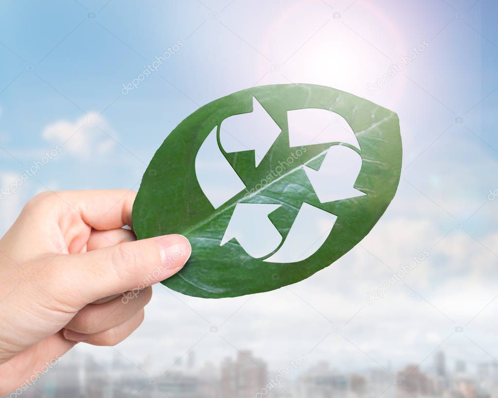 Concept of provide resource recovery, zero waste and green friendly technology, female hand holding a leaf with hole of recycling symbol, on sunlight sky background.