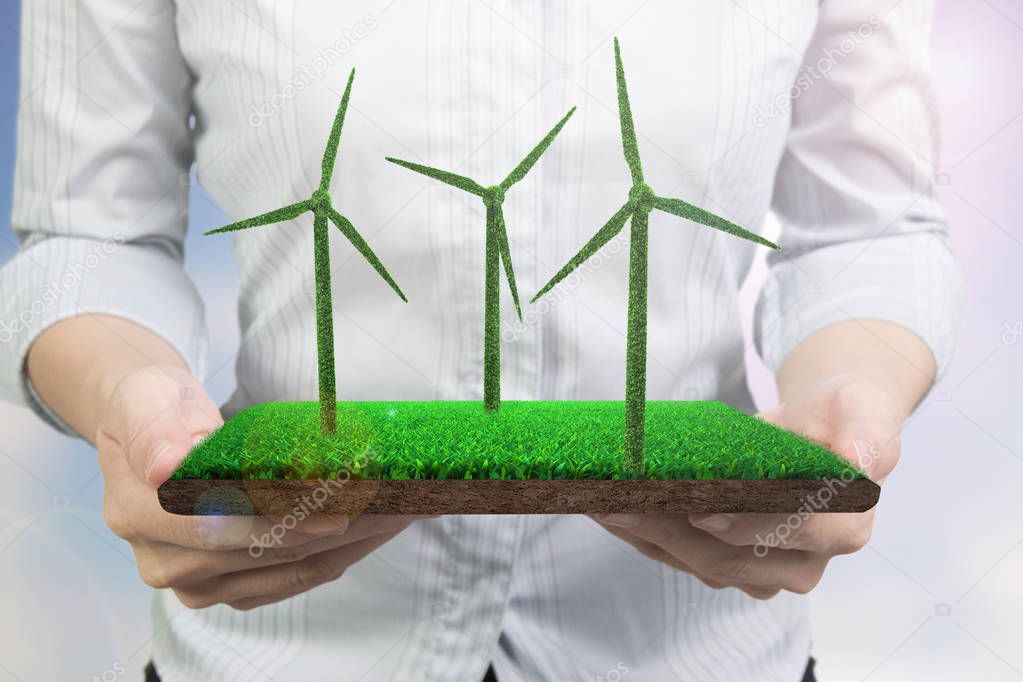 Green energy supply and solution concept, woman hands holding a turf tile with grass in wind turbines shape, front view.