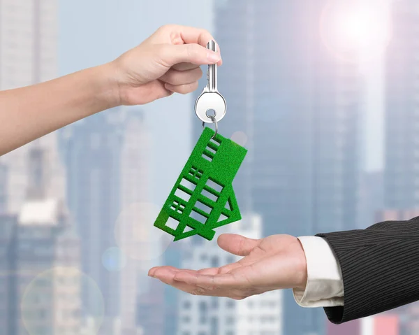 Woman hand giving key with green grass house keyring — Stock Photo, Image