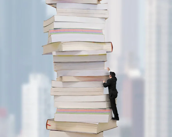 Високий стек книг з бізнесменом, що піднімається на нього — стокове фото