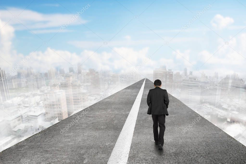Businessman walking on asphalt road in sky with clouds cityscape