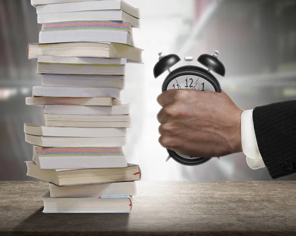 La mano del hombre agarrando el despertador a la deformación con los libros de pila . — Foto de Stock