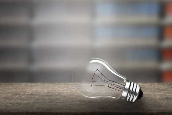 Una lampadina su scrivania in legno, sfondo sfocato libreria — Foto Stock