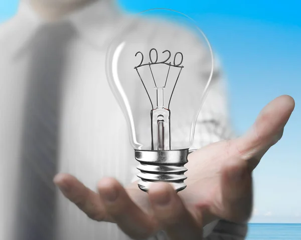 Man palm holding light bulb with 2020 wire shapes — Stock Photo, Image