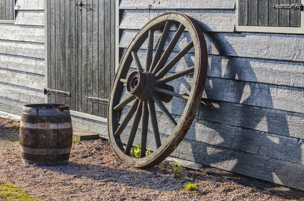 一个生锈的旧车轮和一桶附近的谷仓的墙上的图像 — 图库照片