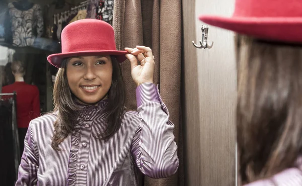 身穿红帽的年轻女子在服装店装修房间 主要集中在镜子里 — 图库照片