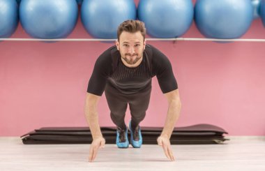 Image of a young handsome man clapping his hands while he is doing pushups in a gym. clipart