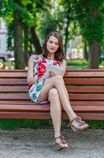 一个年轻女子坐在公园的长椅上使用平板电脑的图片 — 图库照片