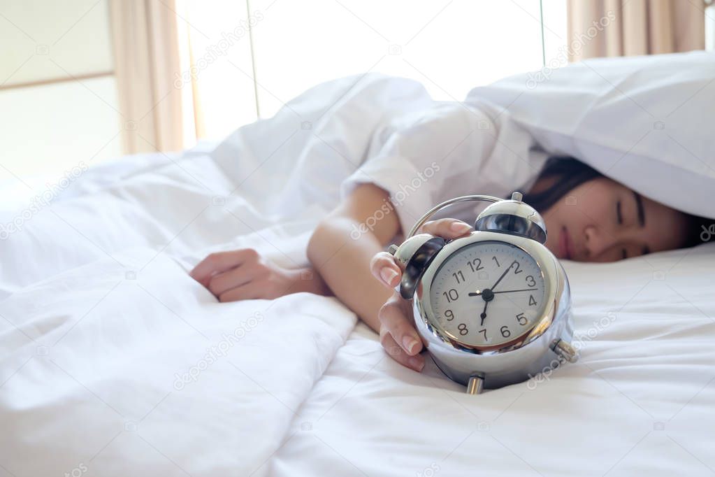 Woman in bed trying to wake up with alarm clock.