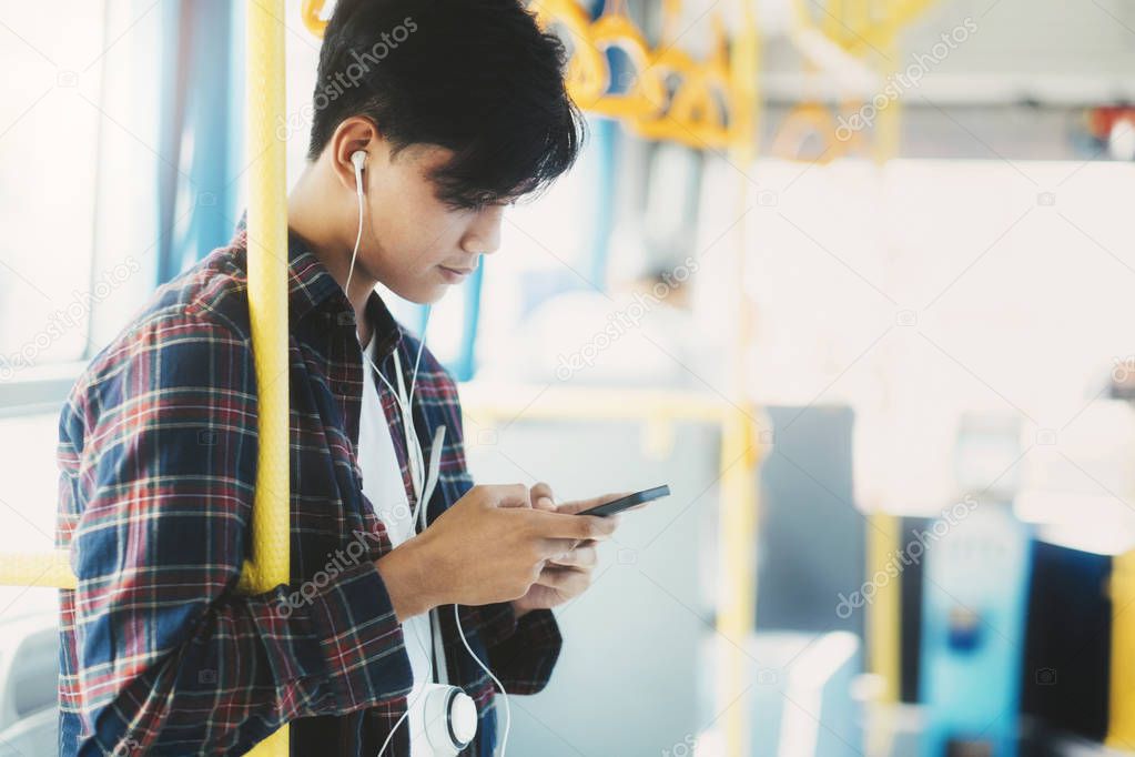 Young asian male passenger using mobile phone on public bus.
