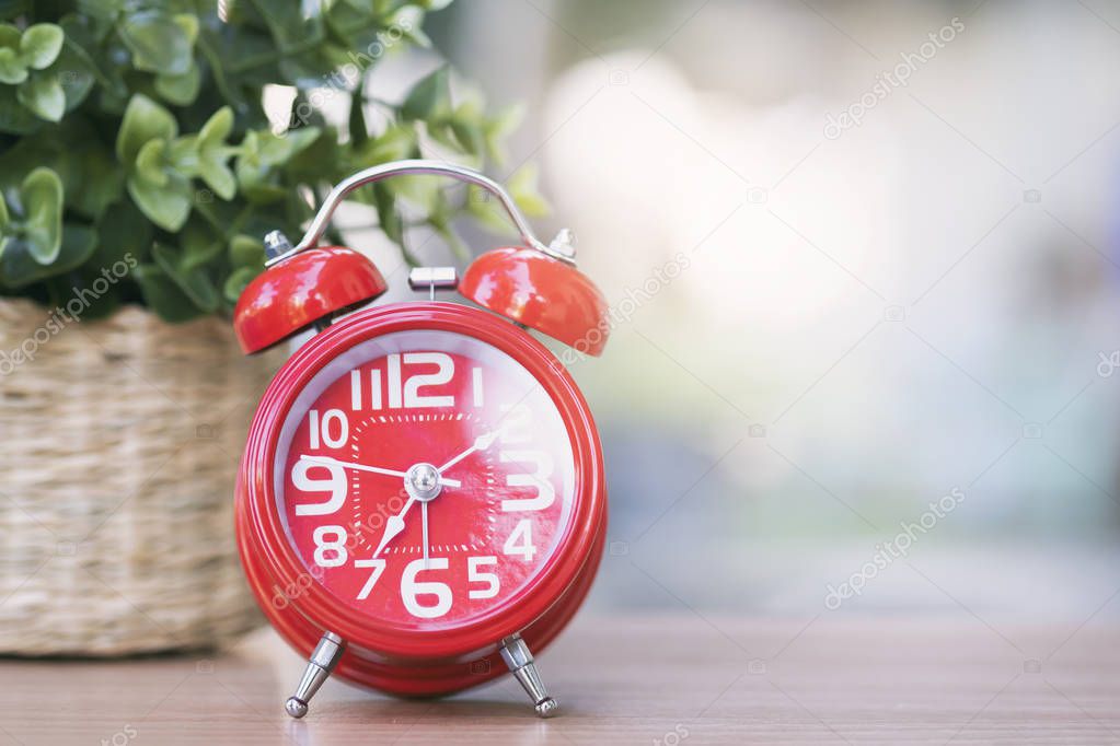 Red clock on wooden table. Starting the new day. Morning time in minimal style decoration. 