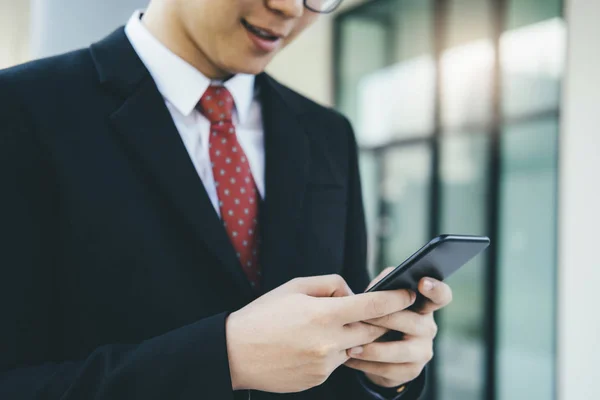 年轻的商人使用手机应用程序在办公室外发短信与摩天大楼建筑的背景 拿着智能手机从事商务工作的年轻人 — 图库照片