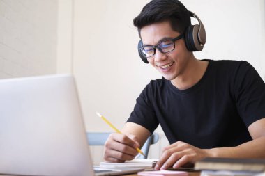 Genç adam evde bilgisayar kullanarak ve internetten öğrenerek çalışıyor.