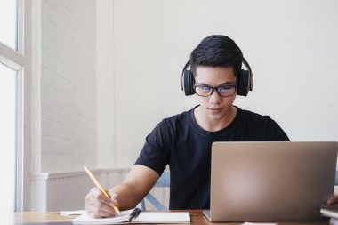 Genç adam evde bilgisayar kullanarak ve internetten öğrenerek çalışıyor.