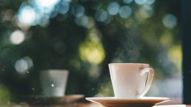 Kahve fincanı ahşap masada ve yeşil bokeh arka planda.