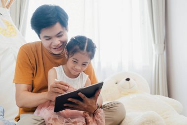 Küçük kız ve genç baba birlikte tablet kullanmaktan zevk alıyorlar. Yaşam tarzı ve aile evde birlikte..