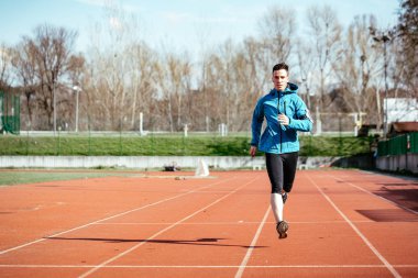 Tartan yolda stadyum üzerinde koşan atletik uygun genç adam