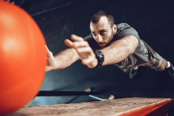 young muscular man doing exercise with volleyball ball at gym