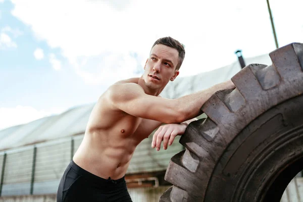 トレーニング筋肉スタジアムに巨大なタイヤを持ち上げる筋肉青年 — ストック写真