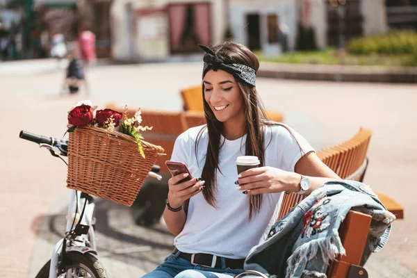 young woman with bike with flower basket using smartphone